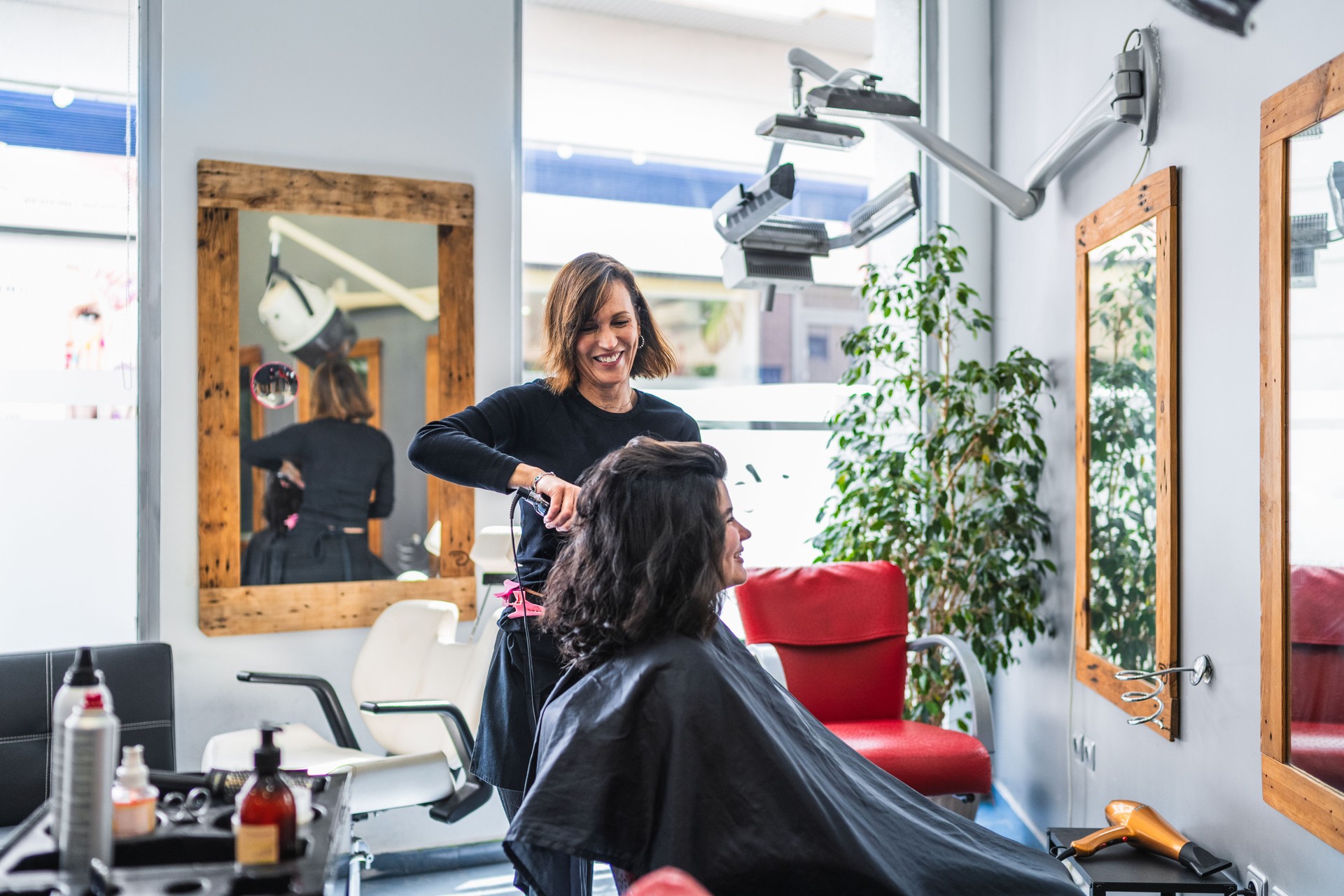 Hairdresser Styling Client's Hair in Modern Salon with Large Mirrors